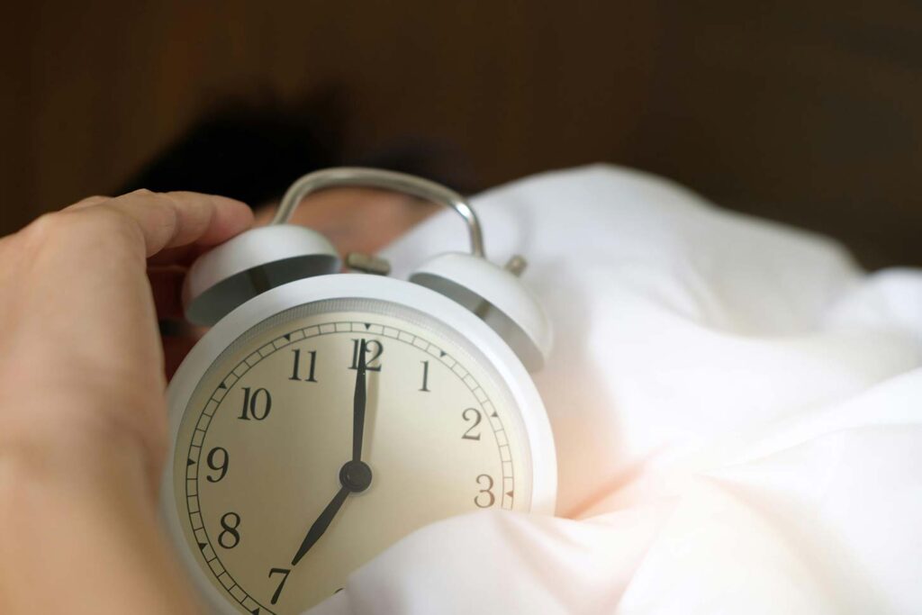 Photo of a person sleeping with an alarm clock